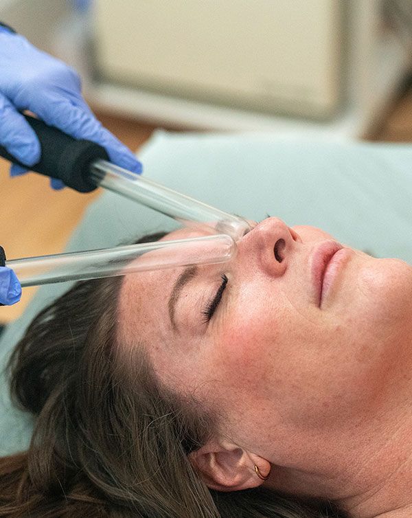 Gloved hands using handheld devices on a woman’s face during a facial treatment
