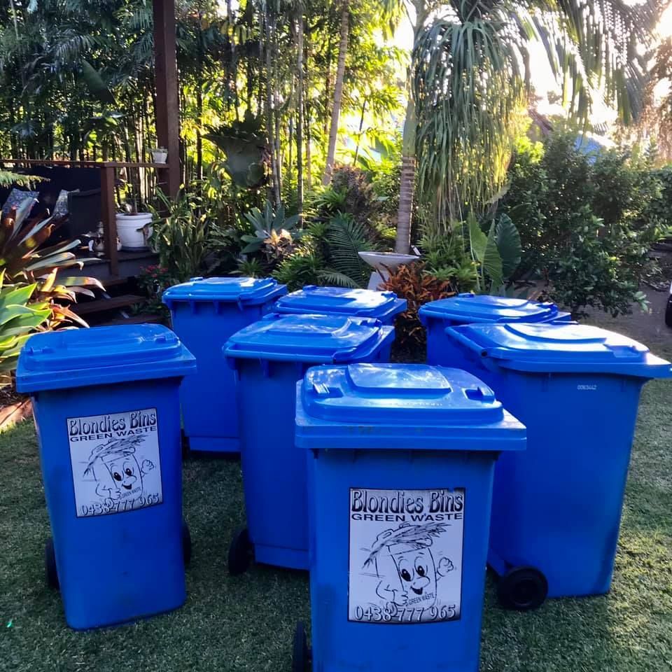 Six Blue Trash Bins With Lids in a Grassy Yard — Blondies Bins in Slade Point, QLD