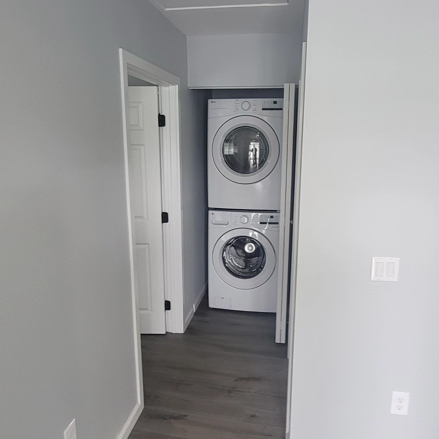 Hallway with stacked washer and dryer in a closet, gray walls and dark wood floor.
