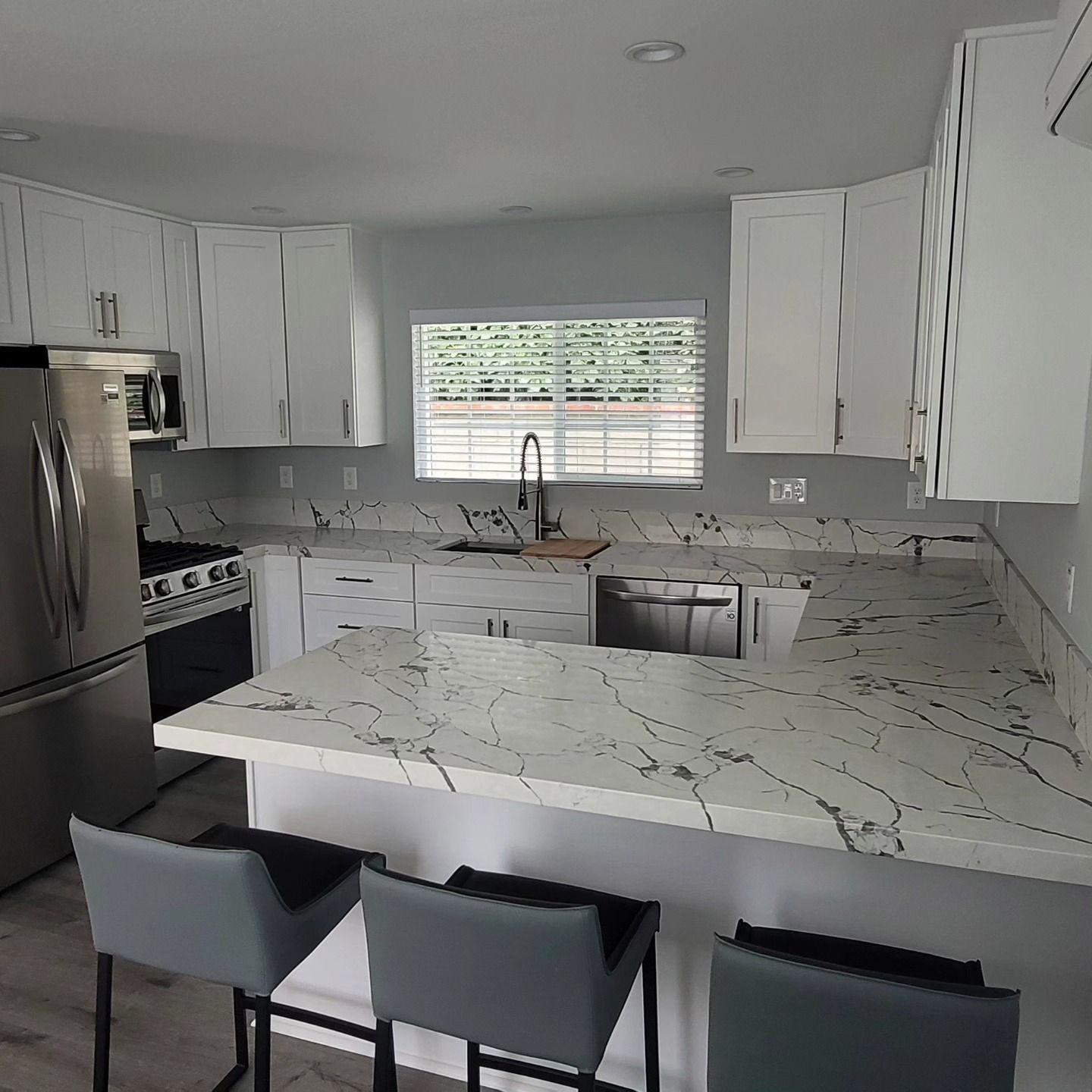 Modern white kitchen with marble countertops, stainless steel appliances, and three bar stools at the island