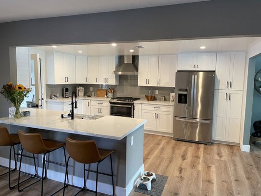 Modern white kitchen with stainless steel appliances, island seating, and light wood floors.