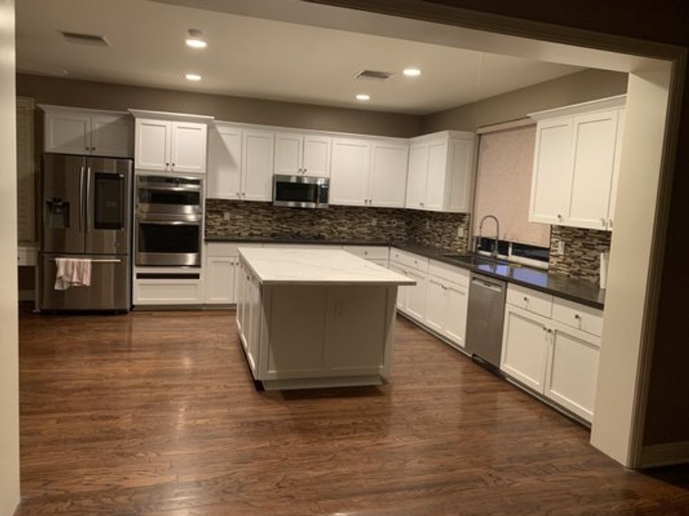 Spacious modern kitchen with white cabinets, stainless appliances, dark wood floors, and a large island