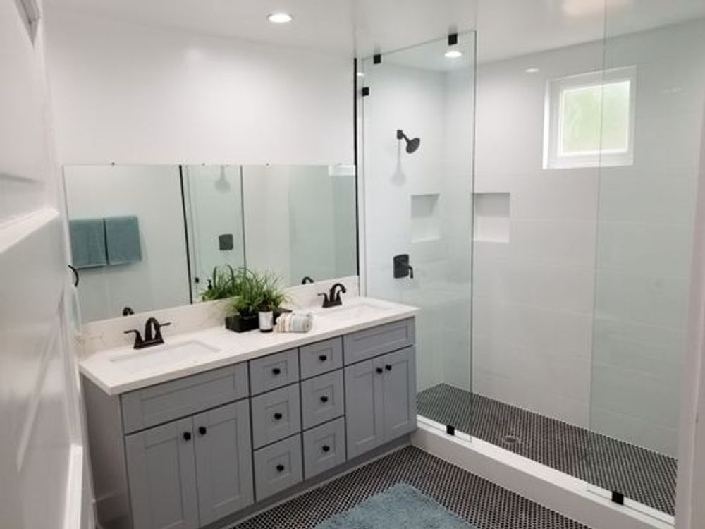 Modern bathroom with gray vanity, double sinks, large mirror, and glass walk-in shower