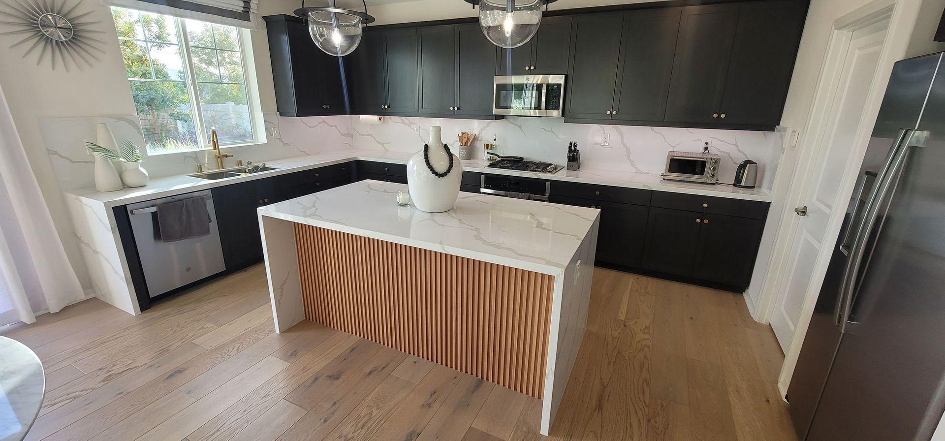 Modern kitchen with white island, wood slatted base, black cabinets, and pendant lights