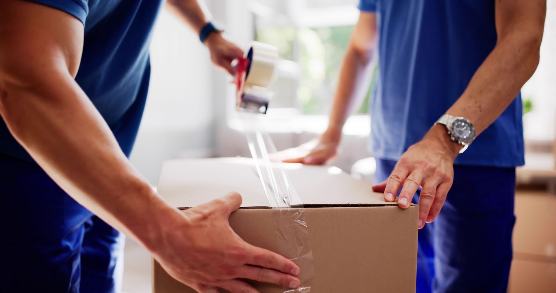 Two men are putting tape on a box.