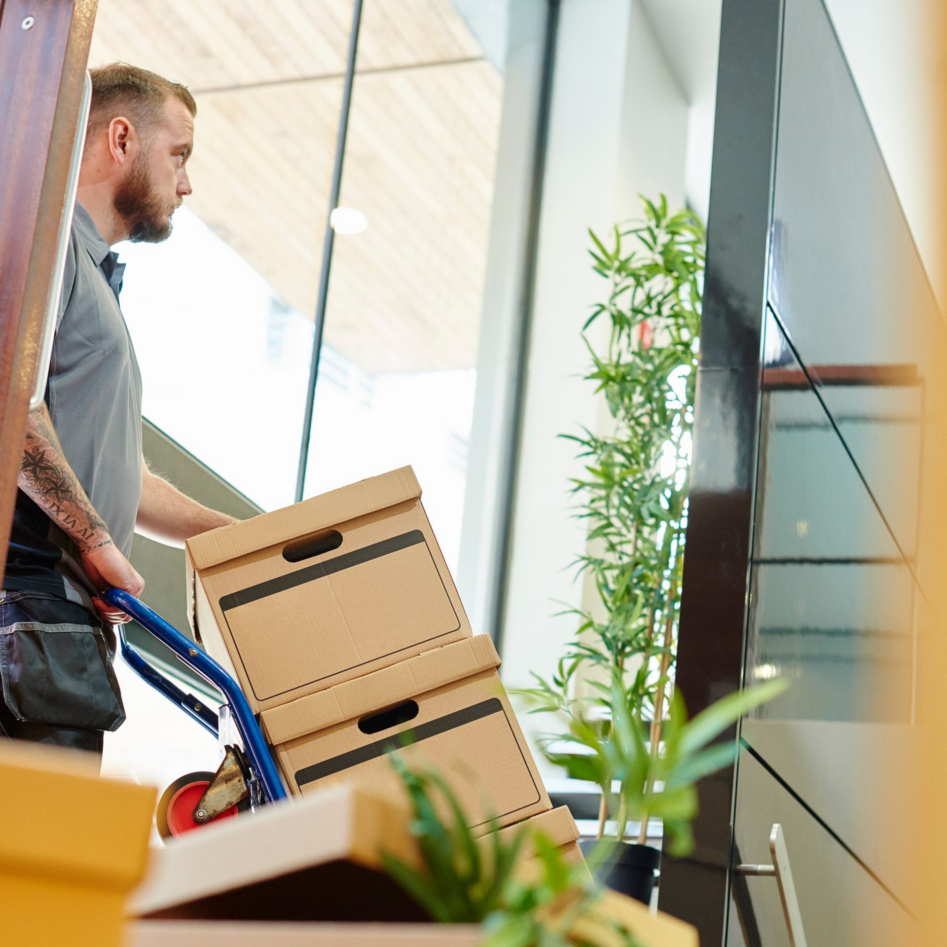 A man pushes a trolley of office boxes through the door of a modern office during a move. A man pushes a trolley of office boxes through the door of a modern office during a move.
