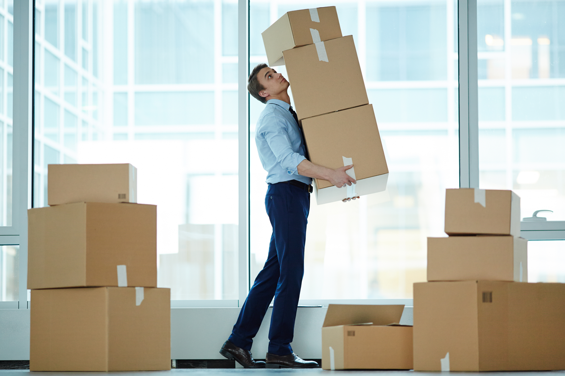 Businessman carrying huge stack of boxes during relocation to modern business center.