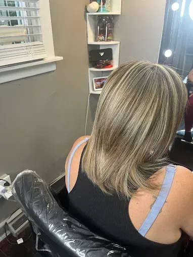 A person with shoulder-length, highlighted blonde hair sitting in a salon chair.