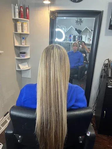 Person in a blue sweater sitting in a salon chair with long, highlighted blonde hair, reflected in a mirror.