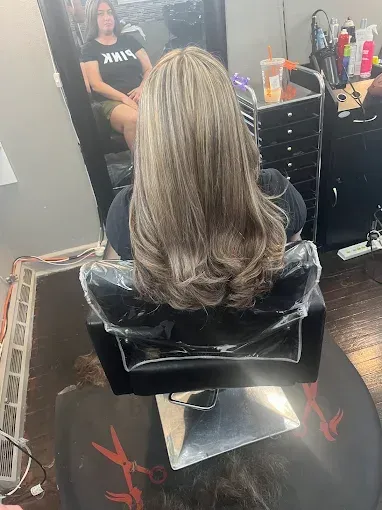 A person sitting in a salon chair shows off shoulder-length, layered, highlighted brown hair with a blow-out style.