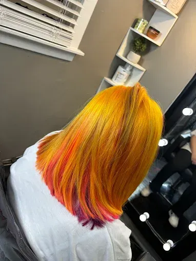 A person’s shoulder-length hair dyed in a gradient of bright yellow, orange, pink, and purple at the tips in a salon.