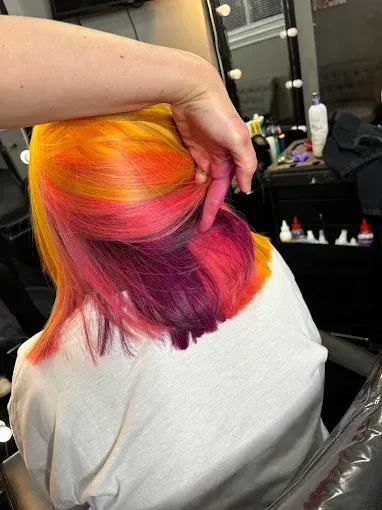A person’s hands style shoulder-length hair featuring horizontal layers of vibrant yellow, orange, hot pink, and purple.
