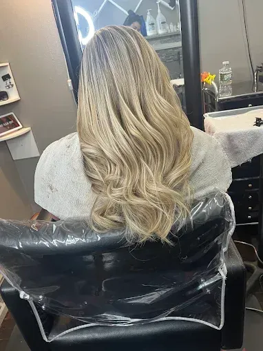 A person sits in a salon chair with long, wavy, blonde-highlighted hair reaching their mid-back.