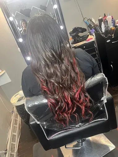 A person with long, dark wavy hair featuring vibrant red highlights at the ends, sitting in a salon chair.