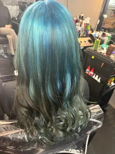 A person's shoulder-length hair styled in a teal to dark green ombre, shown from behind in a salon setting.