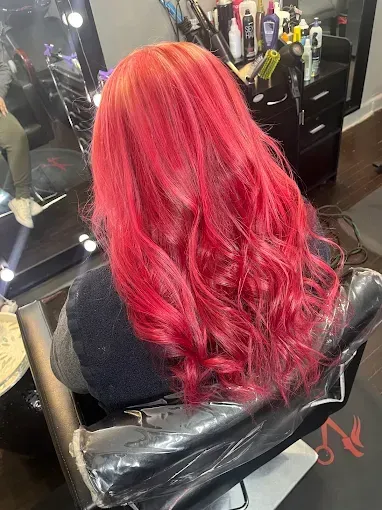 A back view of long, wavy hair colored a vibrant, bright red in a salon setting with hair styling products on a shelf.