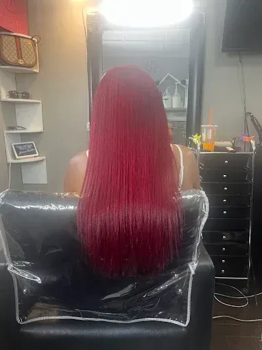 A person with long, straight, bright red hair sitting in a salon chair facing a mirror.