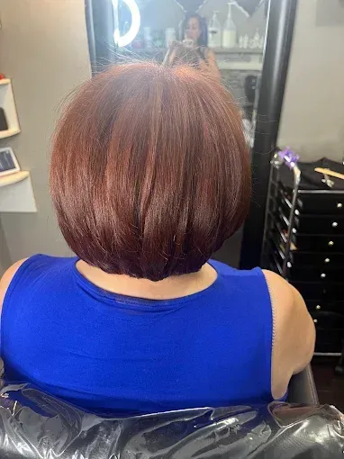 A person with a reddish-brown, chin-length bob haircut seen from behind, sitting in a salon chair.