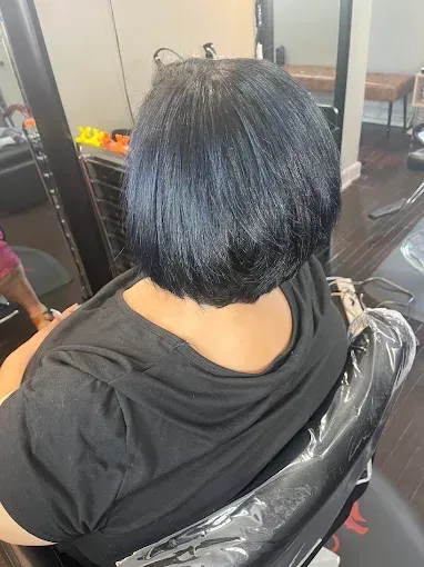 A person sits in a salon chair, showcasing a short, smooth, dark bob haircut viewed from behind.