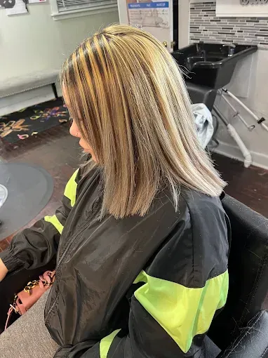 A person with a blonde and brown-highlighted shoulder-length bob hairstyle wearing a black and neon yellow jacket.