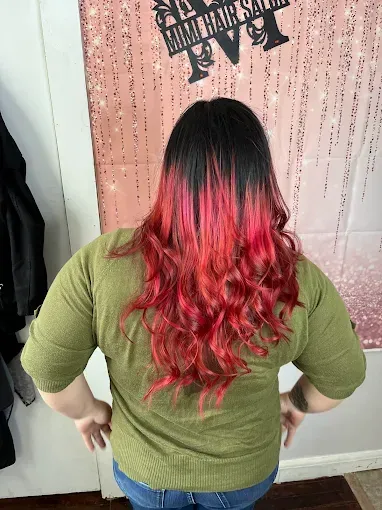 A person with long, wavy hair transitioning from black at the roots to a vibrant, bright red at the ends.