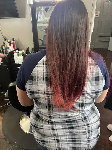 Back view of a person with long, straight brown hair that transitions to a bright red ombre at the tips, in a salon.