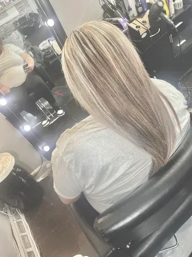 A person sitting in a salon chair, showing blonde hair with highlights from behind, facing a mirror.