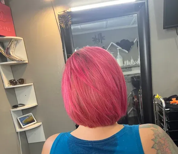 A person with vibrant pink, shoulder-length hair is shown from the back in a hair salon setting.