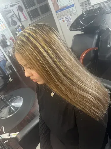 A person with long, straight, highlighted blonde hair sits in a salon chair.