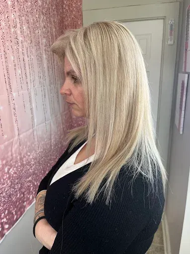 A person with shoulder-length, straight blonde hair stands in profile against a pink decorative backdrop and a door.