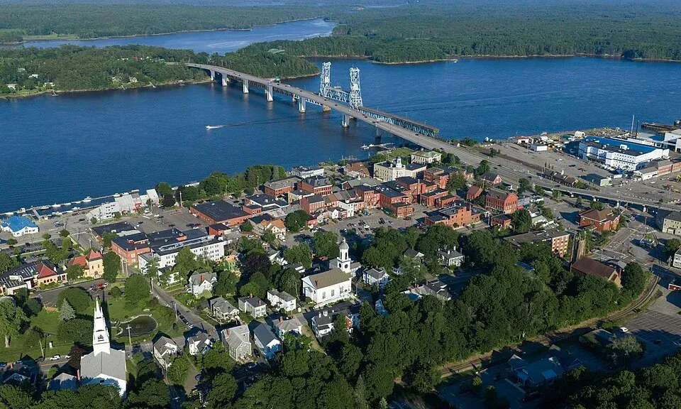 Aerial view of a town by a wide river with a long bridge crossing to the opposite shore
