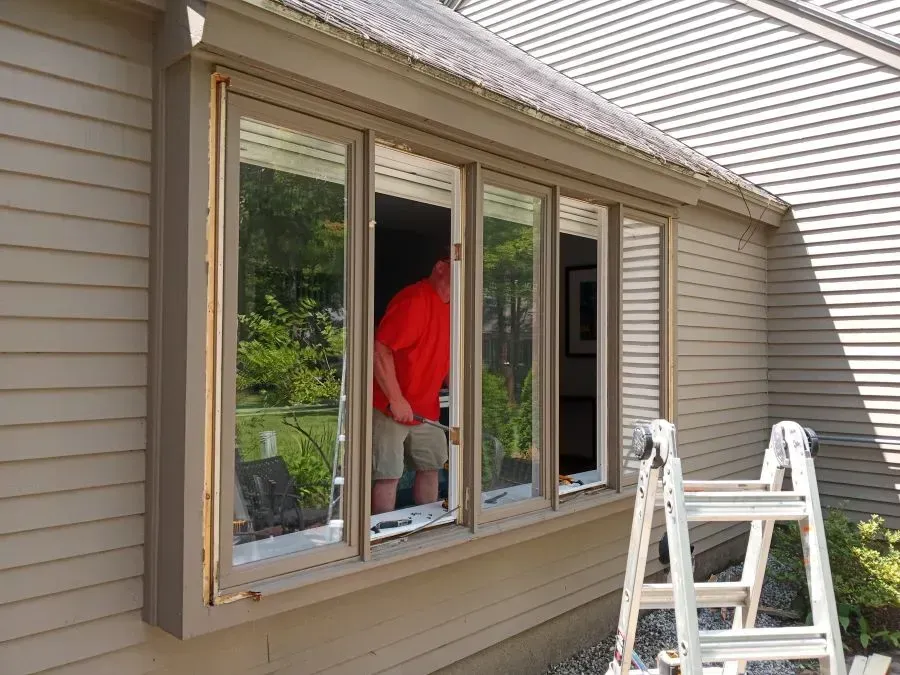 A man is installing a window on the side of a house.