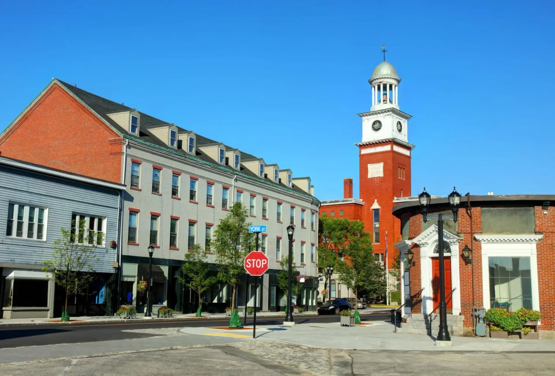 Cobbled town square with historic buildings and a red clock tower under a clear blue sky