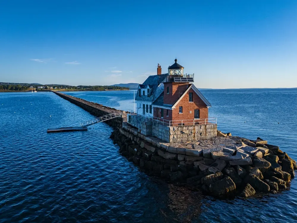 Small red lighthouse on a rocky breakwater in a blue bay under a clear sky