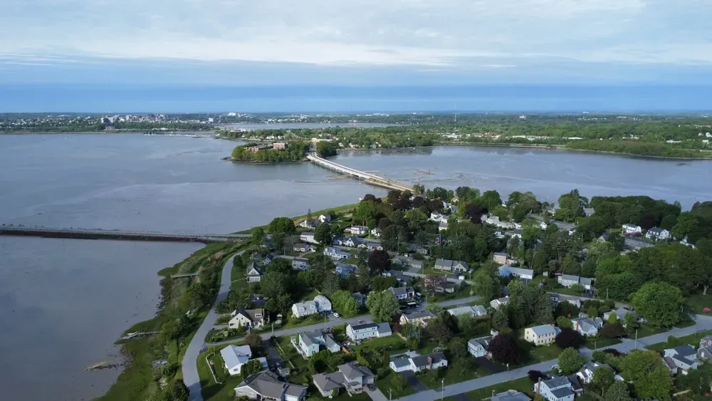 Aerial view of a flooded neighborhood beside wide river water and a bridge under a cloudy sky