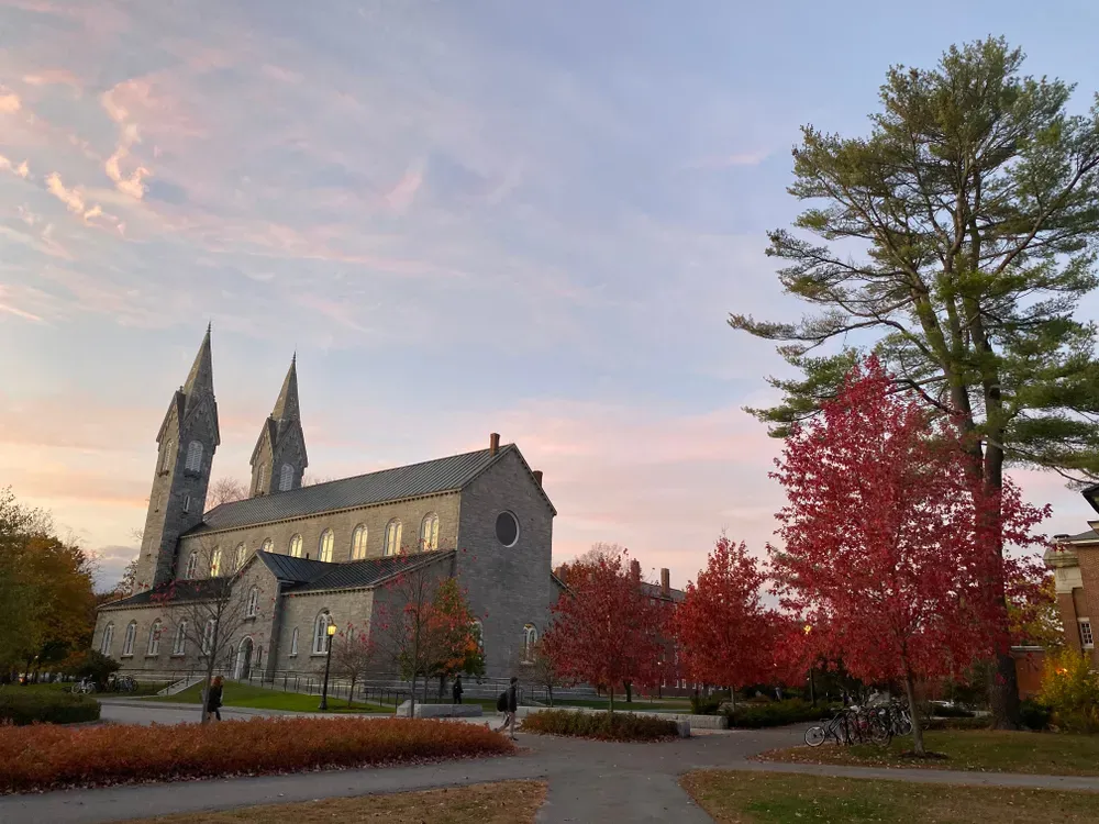 Stone church with twin spires beside red autumn trees at sunset