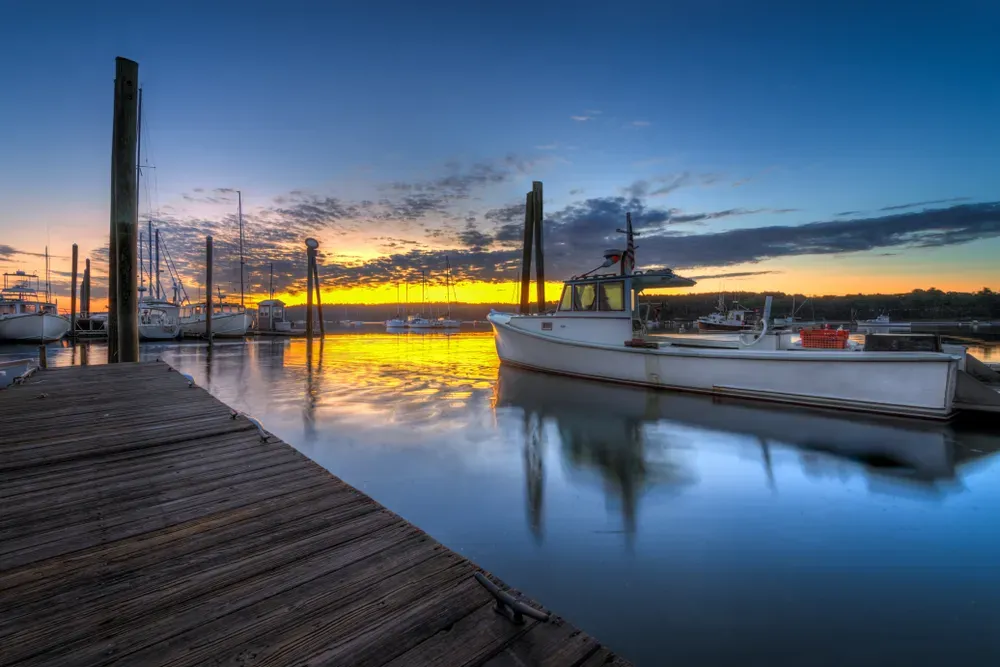 Sunset over a marina with a dock, sailboat, and calm reflective water