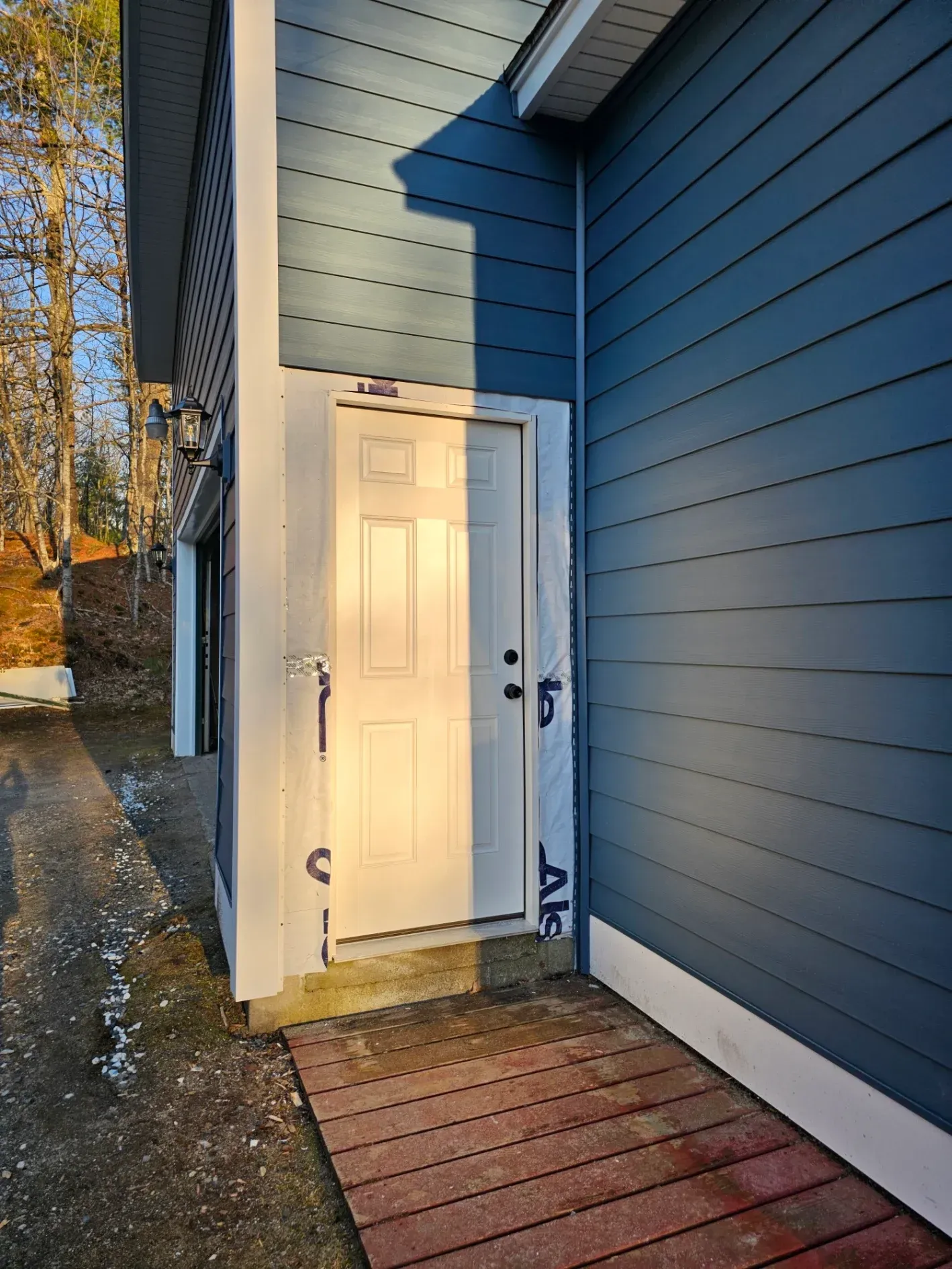 Open white door beside blue house with a small wood porch and gravel path