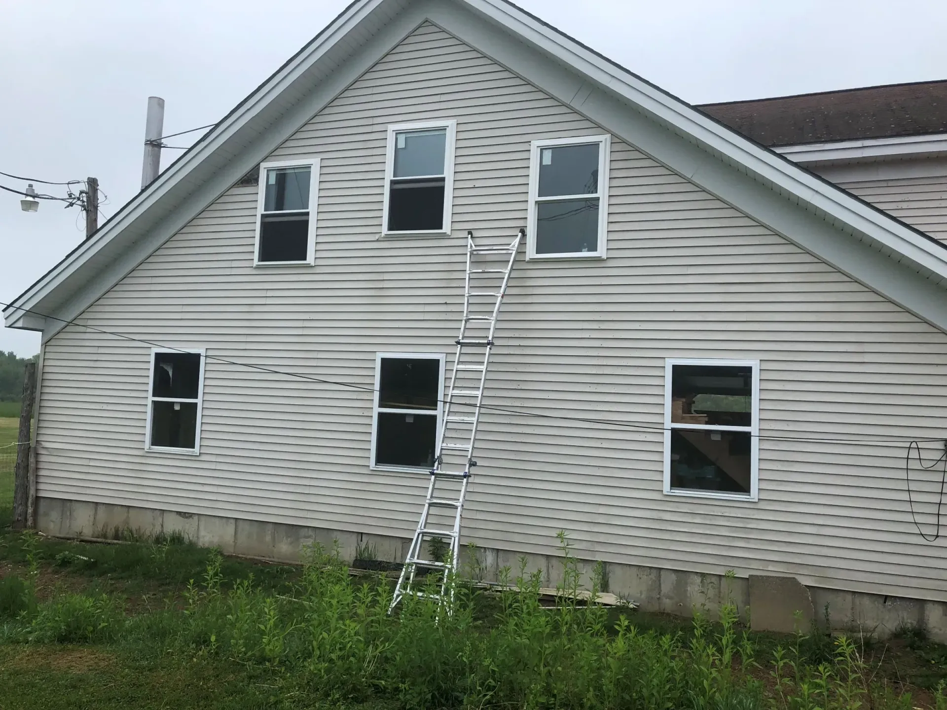 White house with a ladder leaning against it; six windows, siding is weathered.
