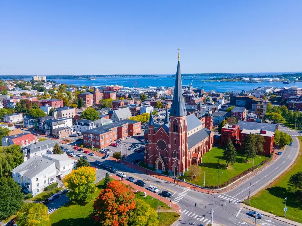 Aerial view of a red-brick church with a tall spire in a coastal town on a sunny day