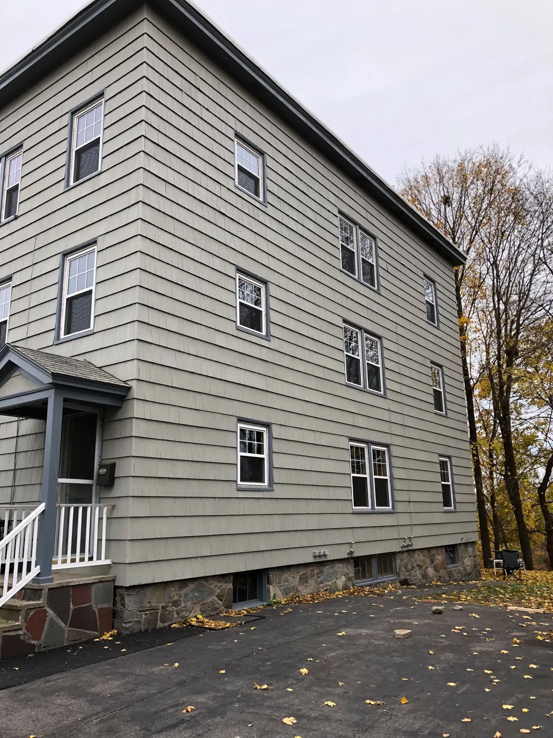 Three-story beige apartment building with white-trimmed windows and a small porch, seen from the side.