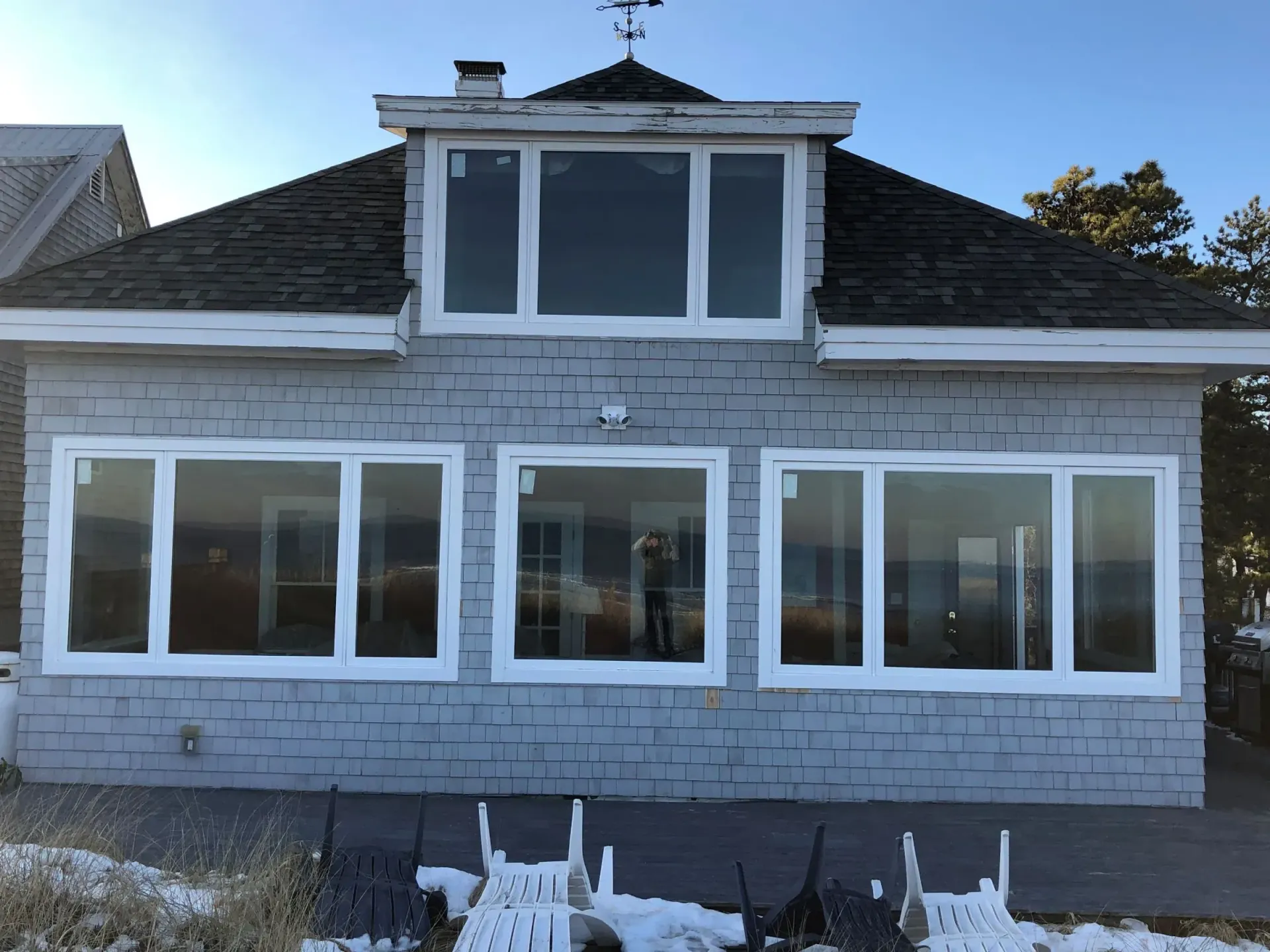Snow-dusted gray house with large white-trimmed windows and dormer under a steep shingled roof