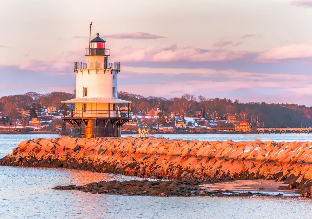 Lighthouse on a rocky breakwater at sunset with pink clouds and calm water