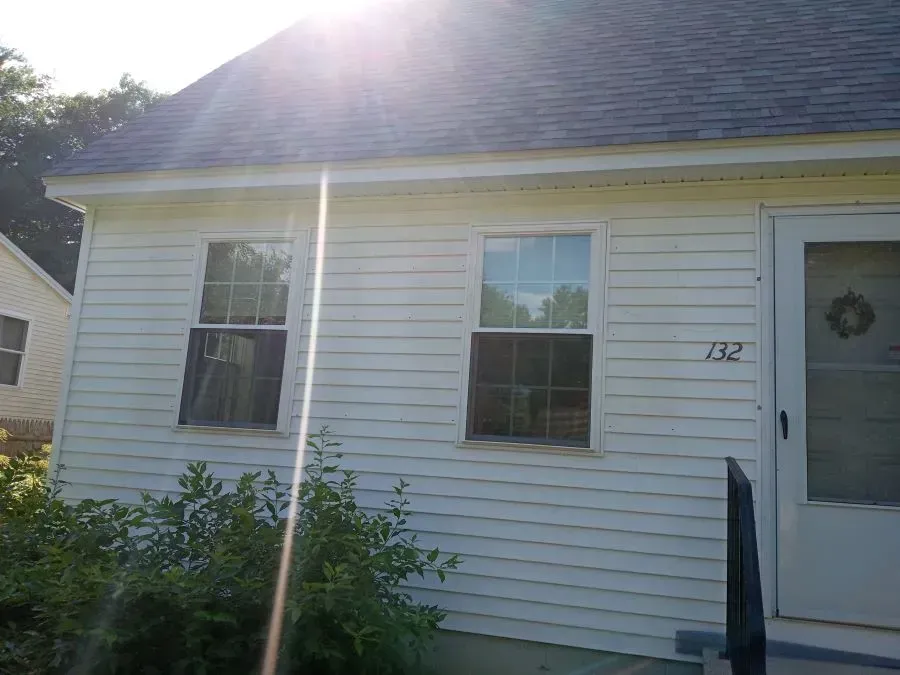Small white house with two windows, front door, and sun glare across the roofline