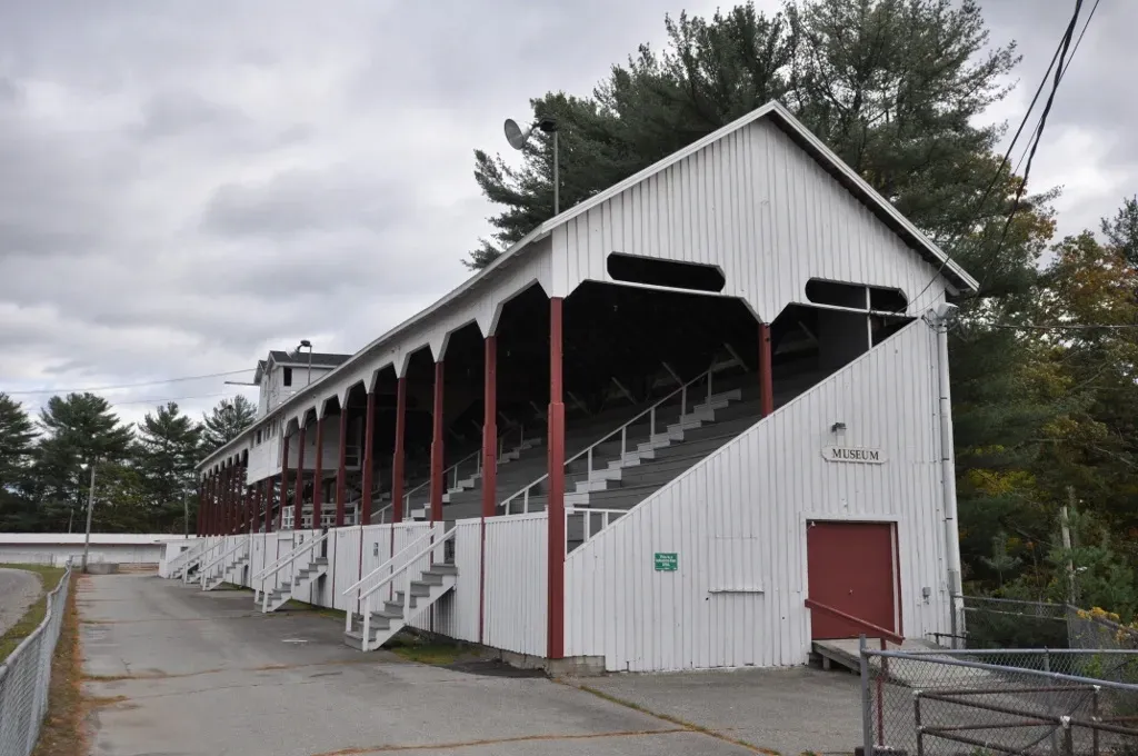 White covered grandstand with red support posts beside a paved lot under cloudy skies