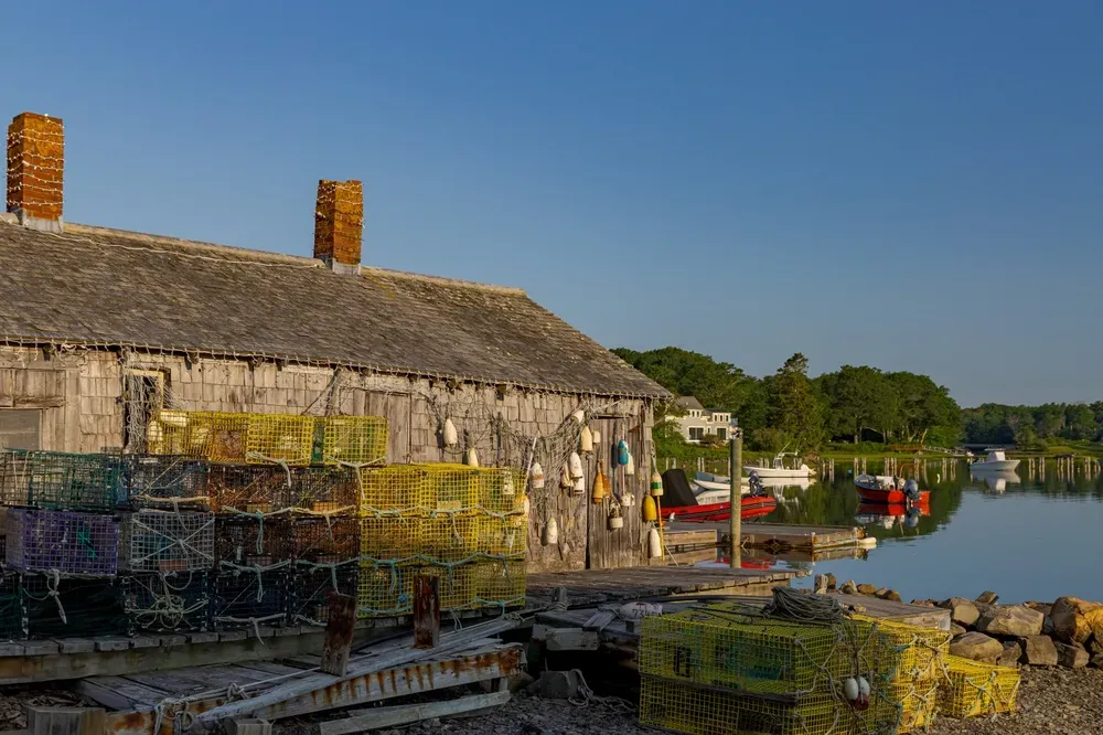 Stone waterfront building beside a calm harbor with moored boats under a clear blue sky