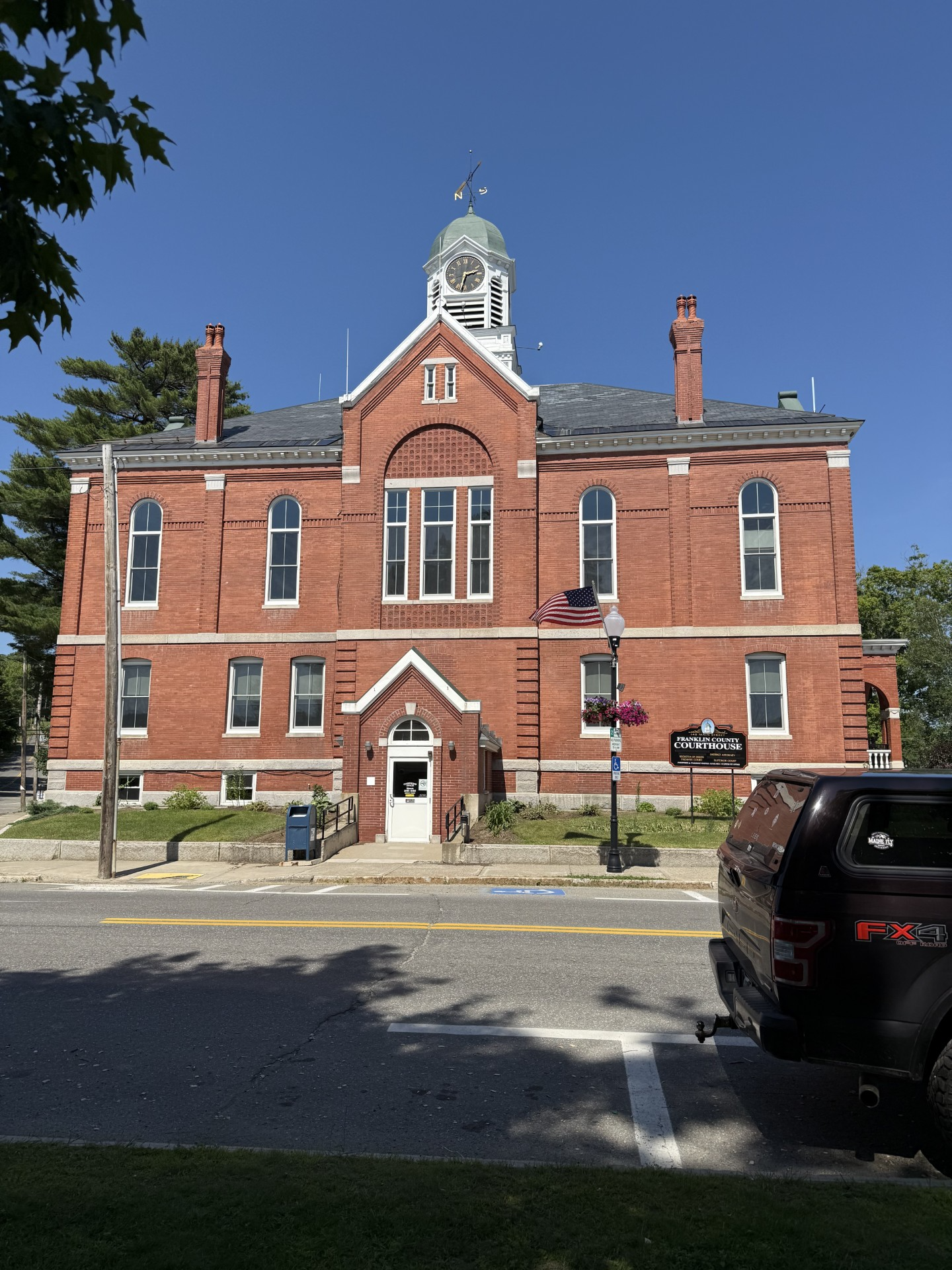 Brick courthouse with clock tower under a clear blue sky. A black truck is parked in front.