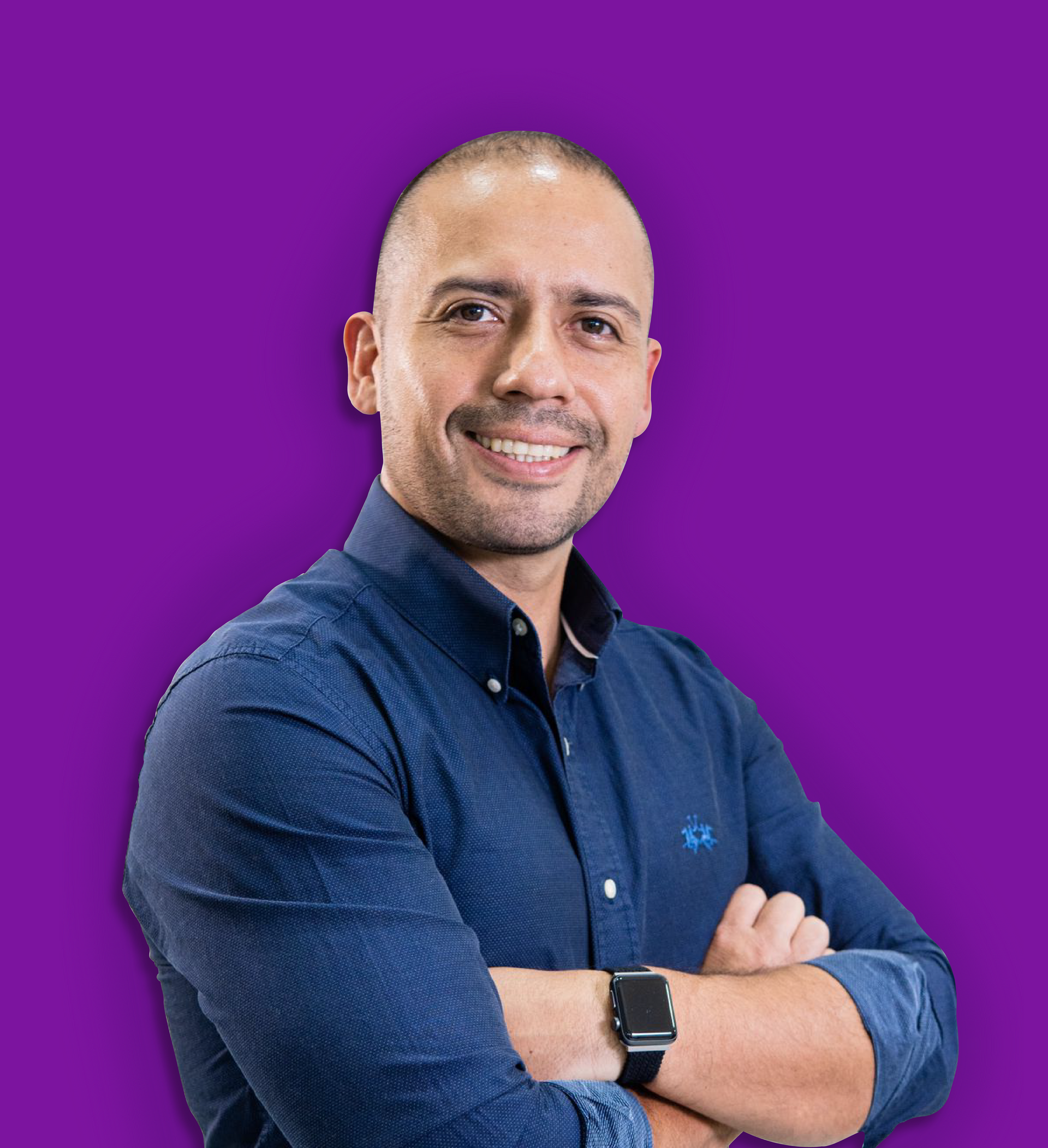 Hombre de pelo corto y oscuro, con camisa azul oscuro abotonada, brazos cruzados y sonriendo. Fondo morado.
