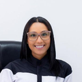 Mujer con gafas sonriendo, vistiendo un top blanco y negro, sentada en una oficina.