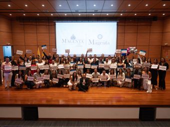 El público observa a una mujer en una pantalla realizando una presentación en un espacio de eventos moderno.